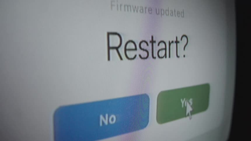 A user clicks 'Yes' on a computer screen to confirm a system restart after a firmware update, and a loading bar shows the progress