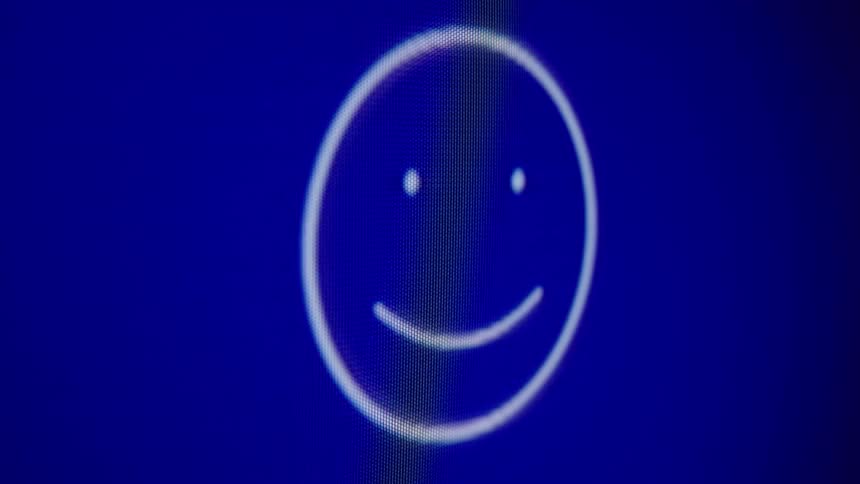 A close-up shot of a looping digital emoji changing expressions from happy to neutral to sad on a blue computer screen