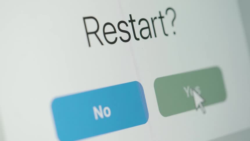 Close-up of a computer screen showing a user clicking 'Yes' to a restart prompt, followed by a system restart progress bar