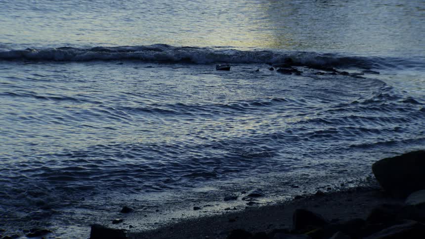 Calm ocean waves gently lap against a rocky shore at dusk