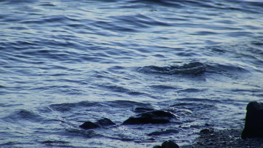 Serene close-up of dark blue ocean water gently washing over coastal rocks in slow motion