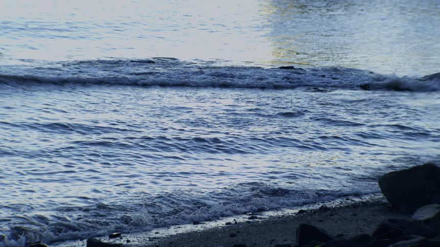 Gentle ocean waves in slow motion lap against a rocky shoreline at dusk
