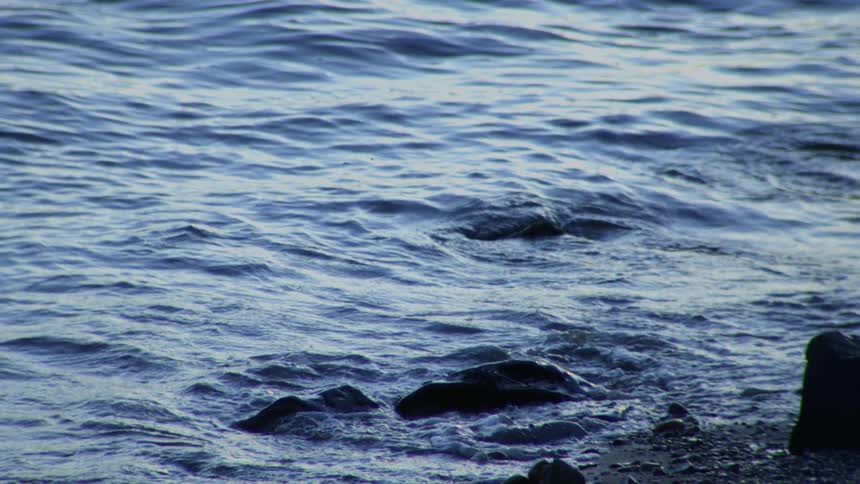 A serene close-up of gentle blue waves lapping against a rocky shoreline in slow motion