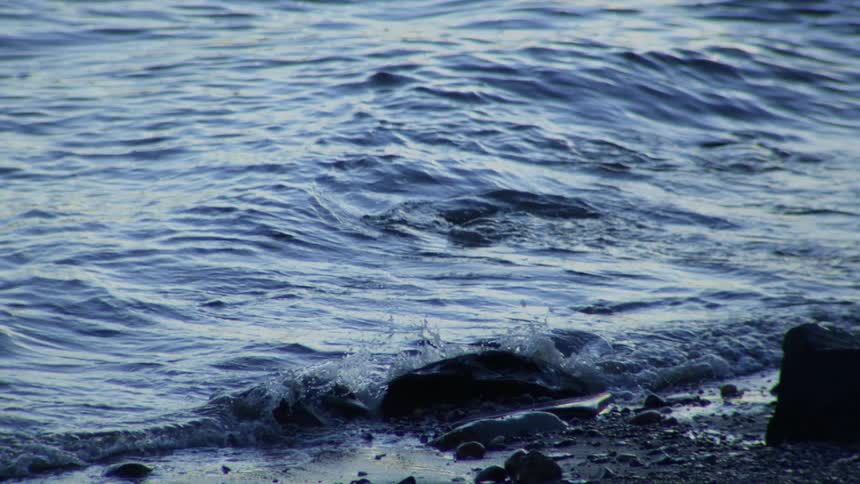 Serene slow-motion close-up of ocean waves gently breaking on a rocky beach
