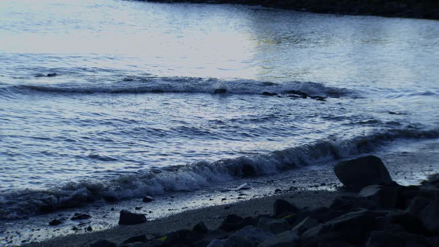 Gentle ocean waves roll onto a rocky shoreline in a tranquil slow-motion cinemagraph