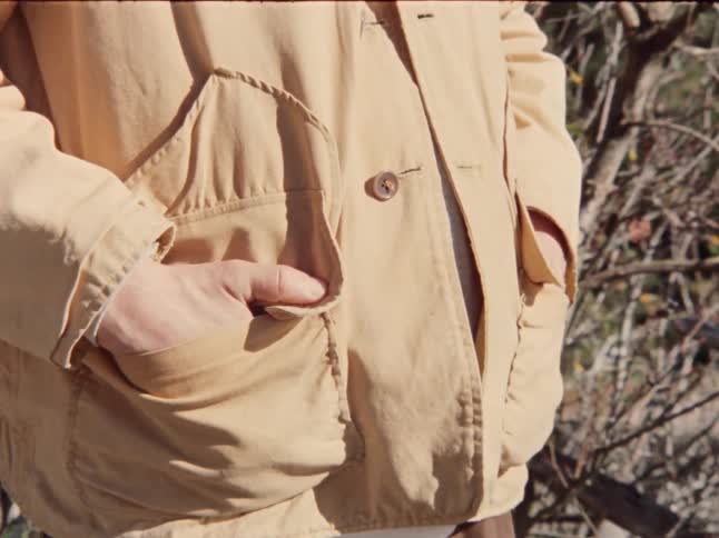 A man stands casually with his hands in his pockets, filmed in a close-up shot outdoors
