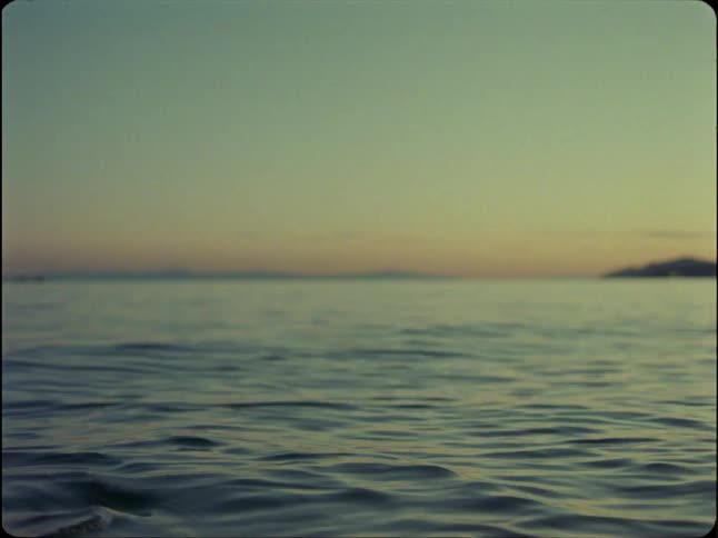 A woman calmly floats in the ocean at twilight, looking at the horizon before the camera focuses on the gentle waves