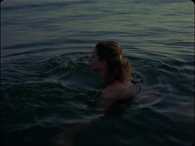 A content woman calmly swims in the ocean at sunset in slow motion, vintage-style footage