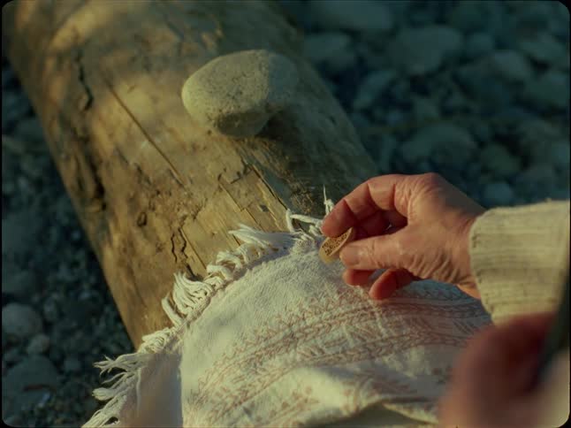 A serene ritual unfolds as a person photographs a wooden token and places it on a stone at the beach