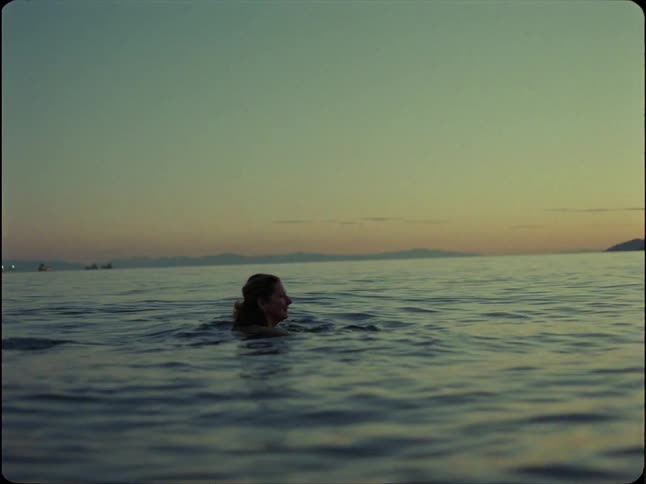 A woman peacefully swims in the vast, calm ocean during a serene twilight, captured in beautiful slow motion