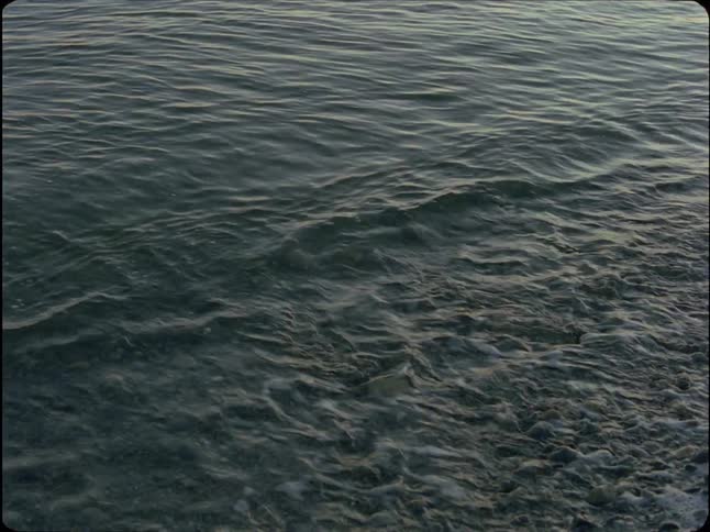 Slow motion shot of gentle ocean waves washing onto a rocky shore