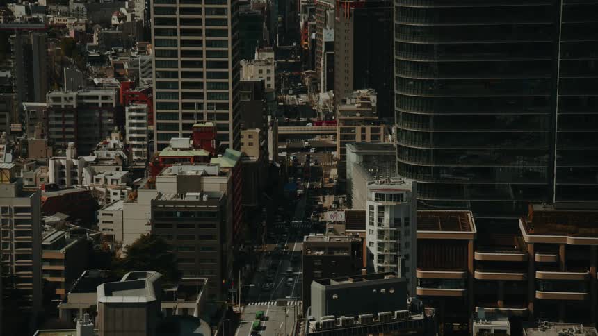 A high-angle view captures the bustling traffic flowing through a street canyon formed by modern skyscrapers in Tokyo