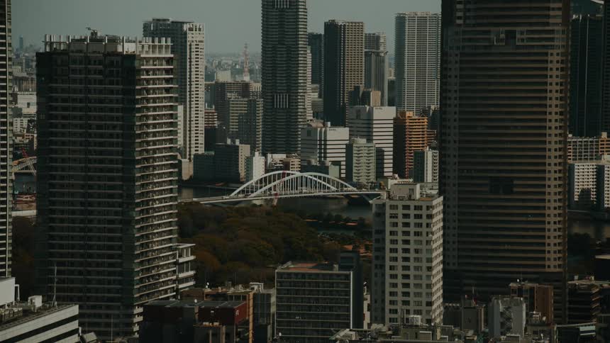 A dynamic timelapse view of a dense modern cityscape, with traffic flowing over a white bridge nestled amongst towering skyscrapers