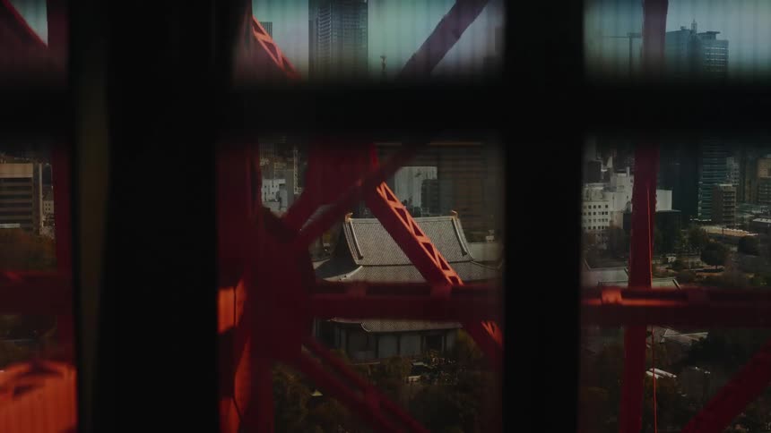 An elevator descends inside the Tokyo Tower, offering fragmented views of the historic Zōjō-ji Temple nestled within the bustling city