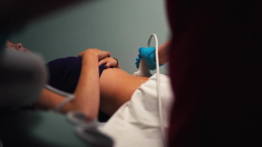 A medical professional uses an ultrasound wand to perform an abdominal examination on a female patient