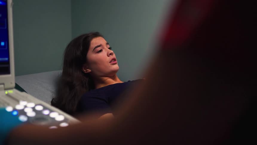 A doctor performs an abdominal ultrasound on a young female patient lying on an examination table