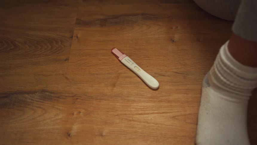 A positive pregnancy test with two lines lies on the wooden floor next to a person's foot