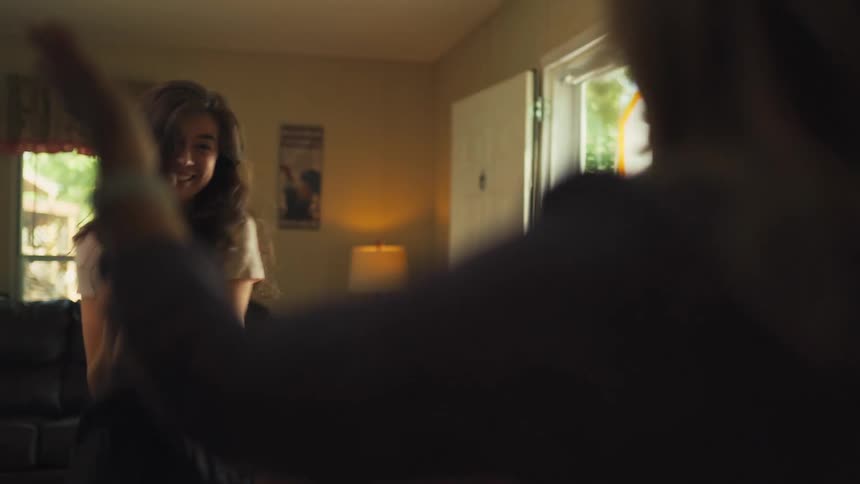 A young woman excitedly reveals a 'Grandma' t-shirt to announce her pregnancy to a family member, who then hugs her in celebration