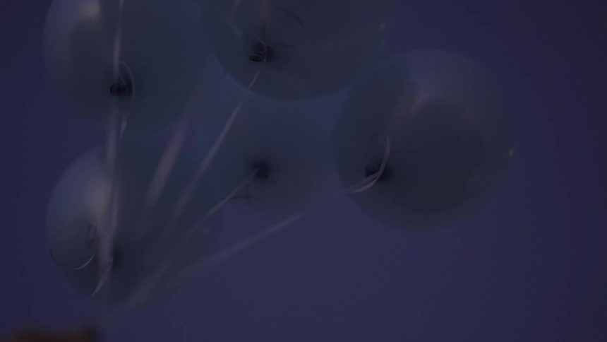 A low-angle shot of light blue balloons held up against the dark evening sky
