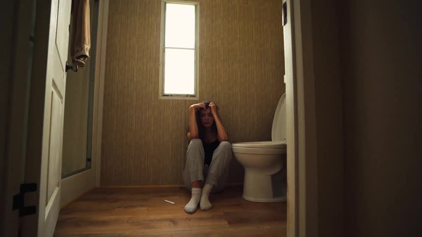 Panning shot reveals a devastated woman crying on the bathroom floor after receiving unwanted pregnancy news