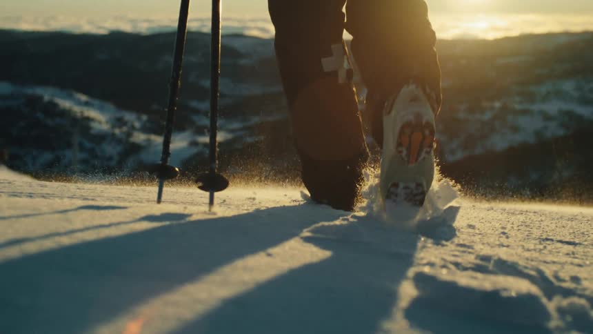 Close-up slow motion of a hiker's boots walking through powdery snow on a mountain during a golden sunset