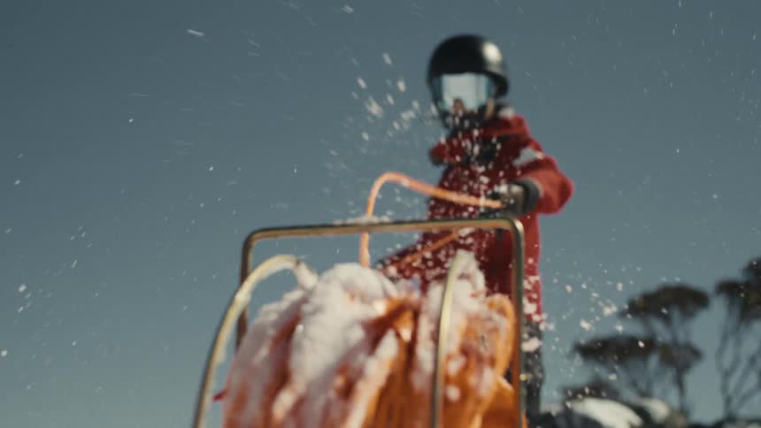 An adventurer in a red snowsuit reels in an orange rope on a snowy mountain, shot in cinematic slow motion