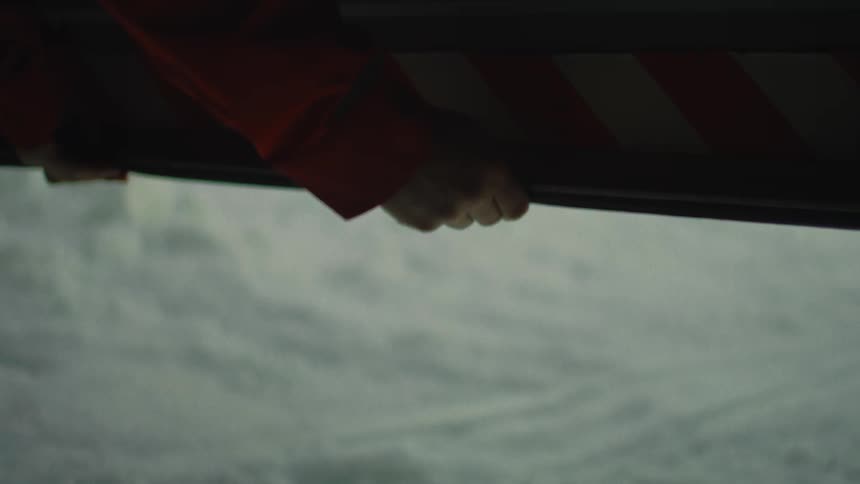 A person in an orange jacket slowly opens the door of a vehicle, revealing a vast and snowy winter landscape outside