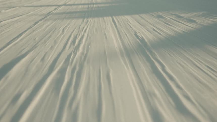 A fast-moving, low-angle shot of wind blowing snow across a frozen, sunlit landscape
