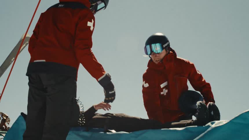 Ski patrol members attend to an injured skier, carefully placing her onto a rescue sled on a sunny mountain