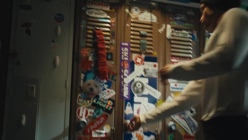 A man opens his locker covered in ski and travel stickers in a rustic locker room