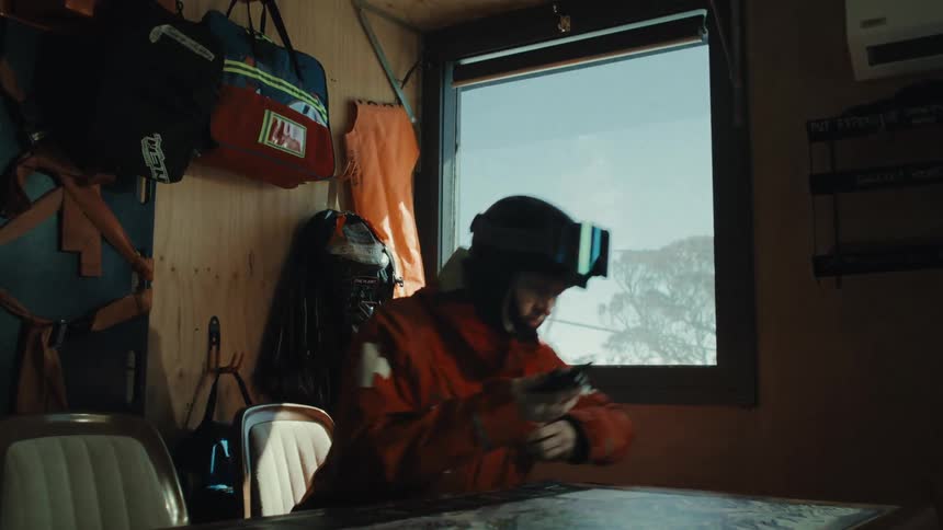 A female ski patroller receives an urgent call in a mountain hut and quickly prepares for a rescue mission