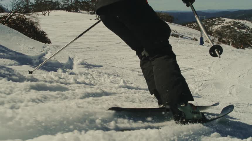 A skier carves down a snowy mountain slope in dramatic slow motion, kicking up powder snow under the bright sun