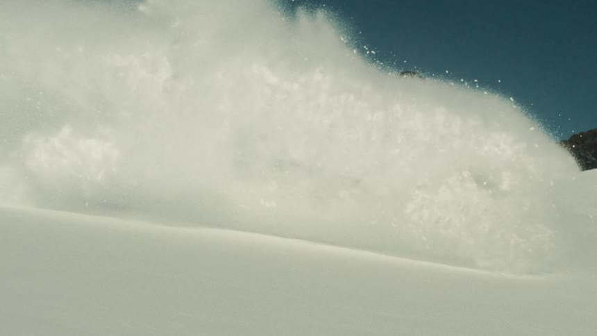 A ski patroller carves a turn in deep powder snow, sending a massive cloud of snow into the air in super slow motion