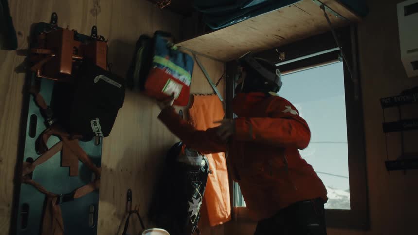 A ski patroller urgently grabs a first aid kit from the wall of a mountain rescue cabin