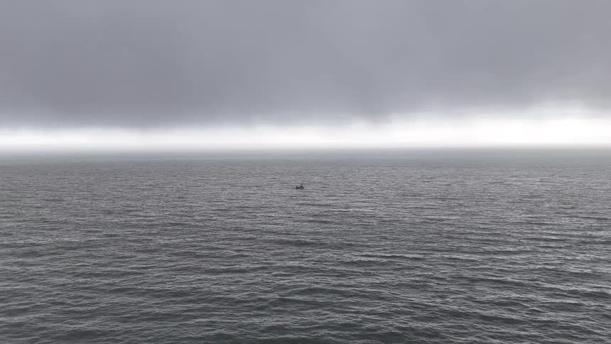 A small, lonely boat drifts on the vast, gray ocean under a thick, foggy sky