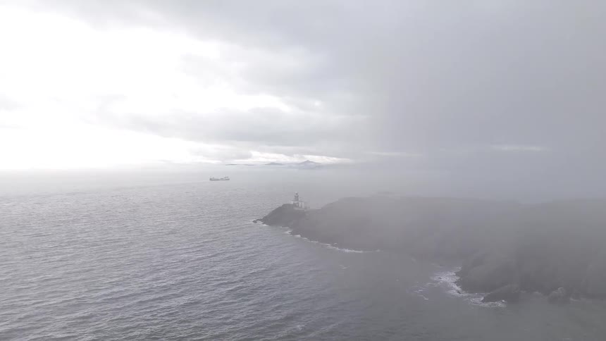 An aerial view of a lighthouse and rocky coastline emerging from a thick blanket of fog