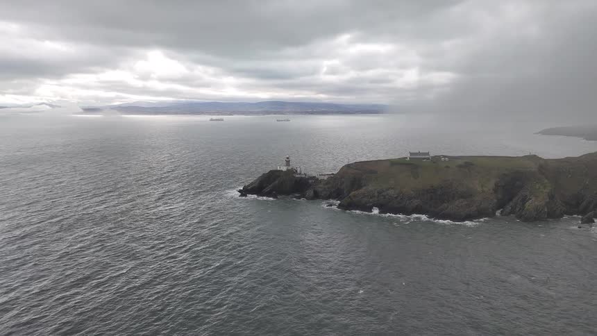 Dramatic aerial shot of a lighthouse on a rocky island being swallowed by a passing rain storm and heavy fog