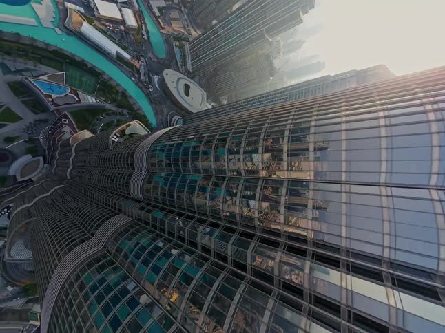 A dizzying top-down aerial shot pans along the glass facade of the iconic Burj Khalifa skyscraper, revealing the cityscape of Dubai below
