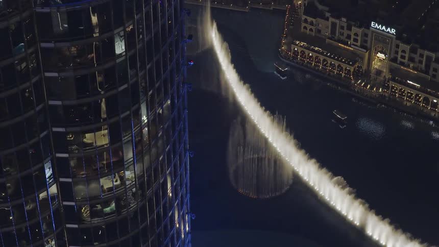 An aerial view from a skyscraper in Dubai at night, showing the spectacular choreographed Dubai Fountain show below