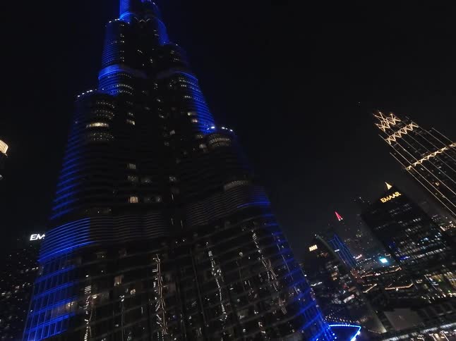 An FPV drone spins and dives down the illuminated Burj Khalifa at night, revealing the dazzling Dubai cityscape