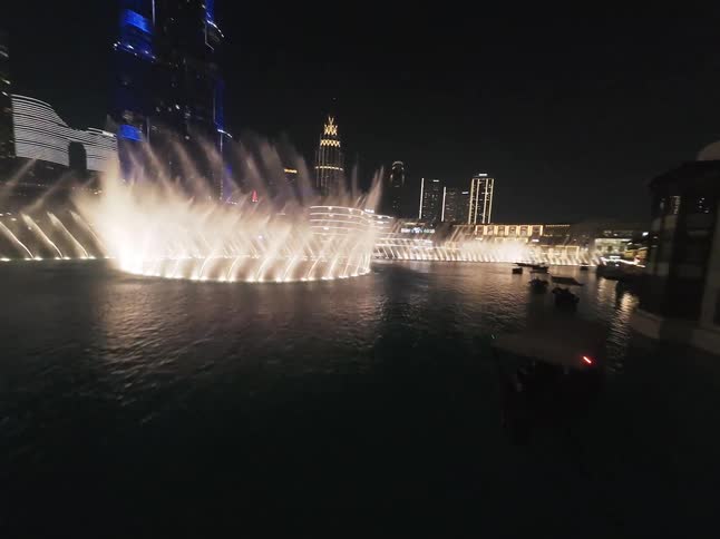 A stunning nighttime aerial view captures the Dubai Fountain show with its illuminated water jets, revealing the dazzling light display on the iconic Burj Khalifa