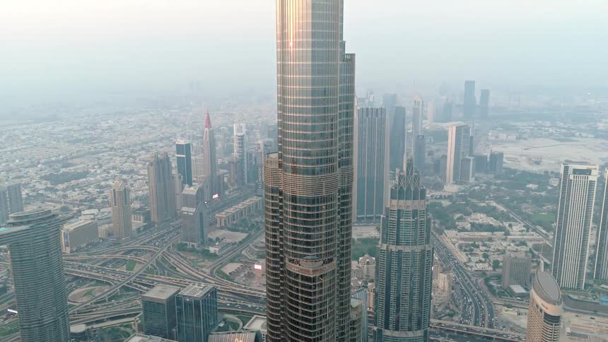 High-angle aerial view of a massive skyscraper towering over the vast cityscape and highways of Dubai