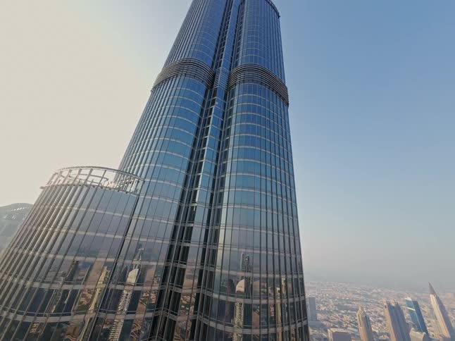 A stunning upward aerial shot reveals the towering glass facade of the Burj Khalifa against the Dubai skyline