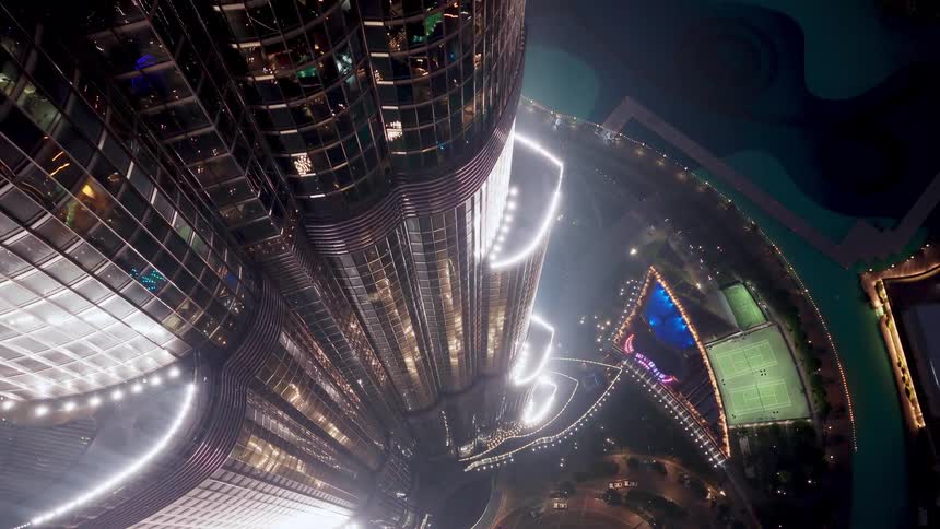 A stunning vertical aerial view looking down the iconic Burj Khalifa skyscraper at night, with the illuminated city of Dubai below