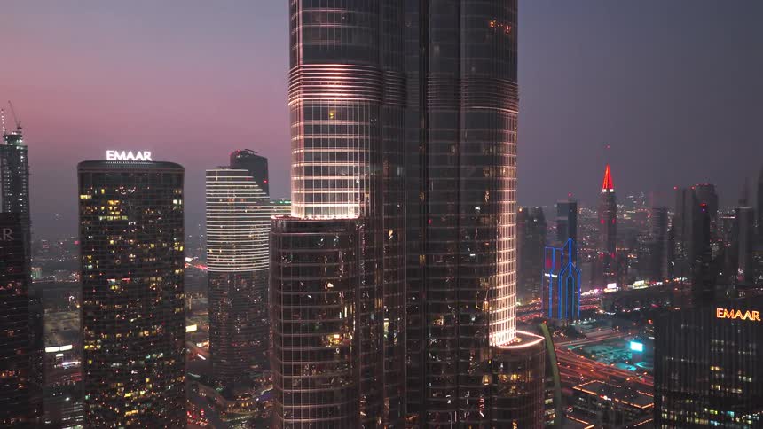 An aerial view of the Burj Khalifa and the surrounding Dubai cityscape illuminated at dusk