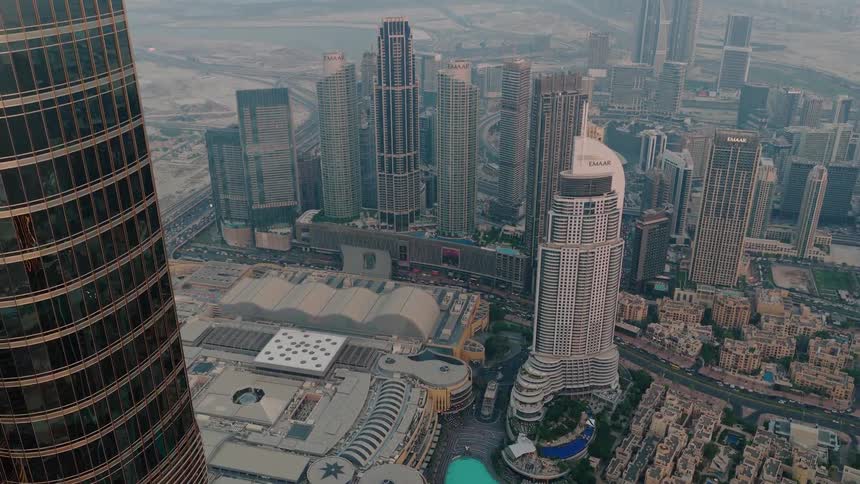 An aerial view from a skyscraper reveals the Dubai cityscape, the Dubai Mall, and the iconic fountains at sunset