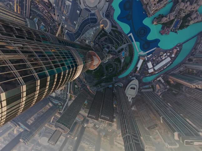 A surreal 'tiny planet' aerial view descends from the top of the Burj Khalifa, revealing the sprawling urban landscape of Dubai below