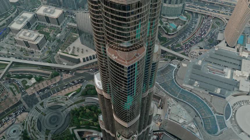 Dramatic top-down aerial view of the Burj Khalifa that slowly pulls back to reveal the incredible cityscape and highway system of Dubai