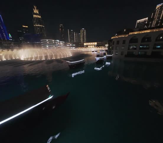 An immersive FPV drone flight over the spectacular Dubai Fountain show at night, with the illuminated city skyline in the background