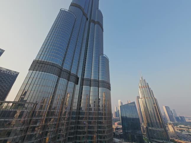 A dramatic aerial shot tilts up the full height of the iconic Burj Khalifa skyscraper, revealing its impressive architecture against the modern Dubai skyline